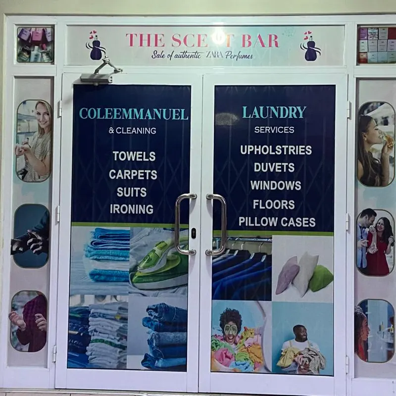 The entrance to the main branch at Sakumono — glazed double doors lettered in navy with the service list: towels, carpets, suits and ironing on one door, upholstery, duvets, windows, floors and pillow cases on the other