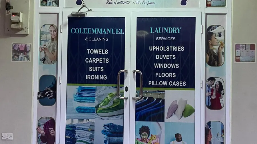The entrance to the main branch at Sakumono — glazed double doors lettered in navy with the service list: towels, carpets, suits and ironing on one door, upholstery, duvets, windows, floors and pillow cases on the other