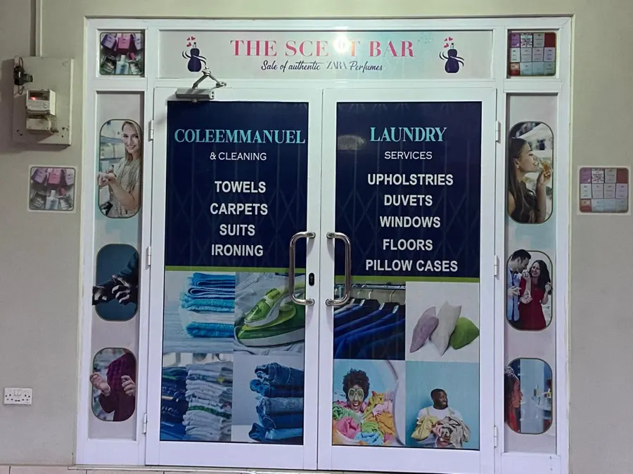 The entrance to the main branch at Sakumono — glazed double doors lettered in navy with the service list: towels, carpets, suits and ironing on one door, upholstery, duvets, windows, floors and pillow cases on the other